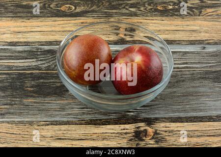 Zwei frische rohe Pluot-Früchte in Glasschüssel auf dem Tisch Stockfoto
