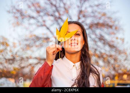 Schöne junge Frau, die Blatt vor ihrem Gesicht hält. Herbststimmung Stockfoto