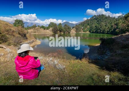 Alleinreisende, alleinreisende Frau, die Deoria Tal mit ihrem Handy fotografiert, Hochgebirgssee in Uttarakhand, Indien. Blauer Himmel mit Schnee Stockfoto