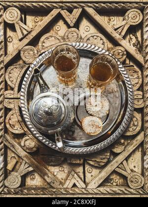 Traditioneller marokkanischer Minztee mit Plätzchen auf silbernem Tablett auf geschnitztem Holztisch. Schöner Vintage-Stil, Gastfreundschaft in Marokko. Stockfoto