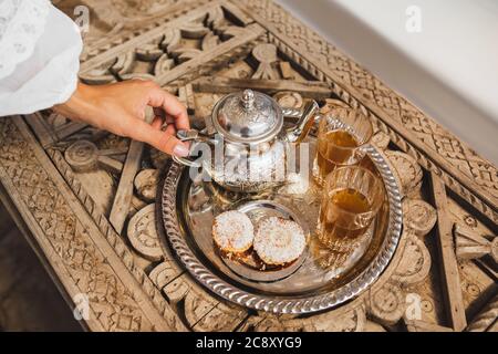 Frau Hände serviert traditionelle marokkanische Minze Tee Zeremonie mit Cookies und vintage Silber Teekanne. Gastfreundschaft und Service in Marokko, Marrakesch. Stockfoto