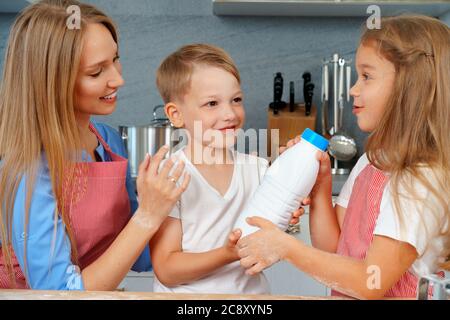 Cute blonde Kinder helfen ihre Mutter in der Küche vorbei Flasche Milch Stockfoto