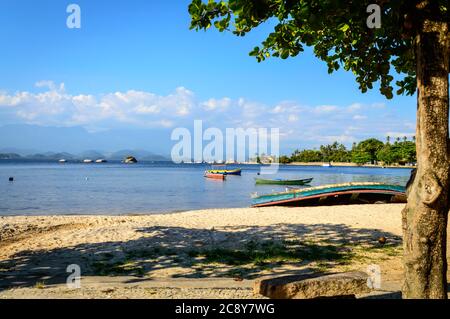 Ruhiger Strand Sene mit bunten Holzbooten, Sand, Schatten, Baum, ruhiges Wasser auf Paquetá Island, Rio de Janeiro, Brasilien. Stockfoto