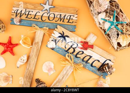 Holzschilder begrüßen Strand, Seesterne und Muscheln auf gelbem Hintergrund. Stockfoto