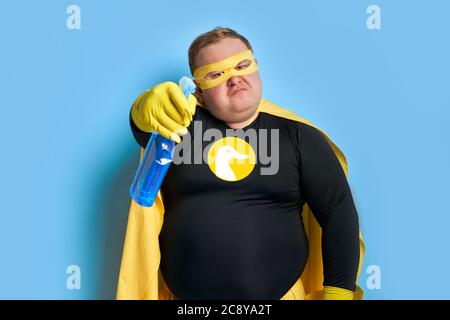 Wütend kaukasischen fetten Mann in gelben Kostüm wendet Reinigungsmittel an der Kamera, er ist müde von Schmutz. Reinigungskonzept Stockfoto