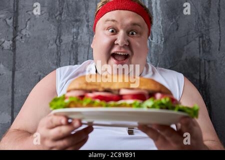 Gut aussehende kaukasischen dicken Mann gehen zu essen große leckere Sandwich, er ist nicht durch sein Übergewicht peinlich, er eata, was er will Stockfoto