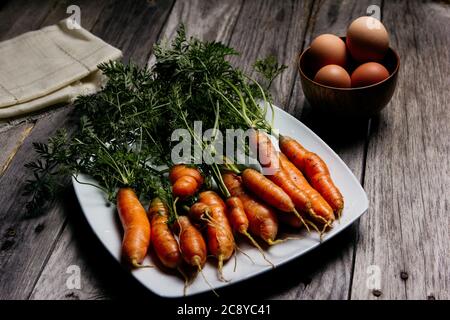 Teller mit Karotten in der Nähe einer Schüssel mit Eiern Stockfoto