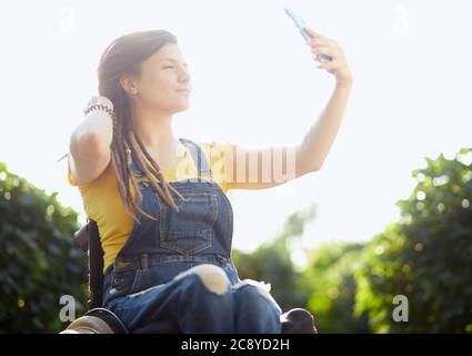 Schönes Mädchen, ein Selfie, während auf dem Rollstuhl im Freien sitzen. Close up Portrait Stockfoto