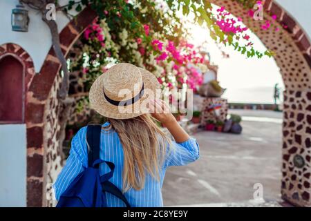 Frau Reisende geht entlang der traditionellen Dorfarchitektur auf Santorini Insel. Tourist bewundert Blumen. Sommer Stockfoto