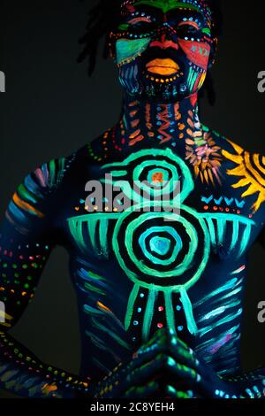 Konzeptuelles Porträt des jungen afrikanischen Mannes in leuchtenden fluoreszierenden UV-Farben gemalt. Make-up, Body Art Konzept, isoliert Studio-Shooting Stockfoto