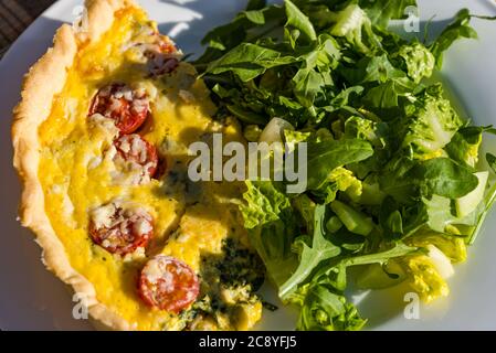 Tisch im Freien mit Sommeressen mit Tomaten, Spinat und Eierteig Quiche lorraine und grünem Salat Stockfoto