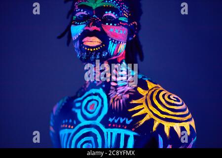 Konzeptuelles Porträt des jungen afrikanischen Mannes in leuchtenden fluoreszierenden UV-Farben gemalt. Make-up, Body Art Konzept, isoliert Studio-Shooting Stockfoto