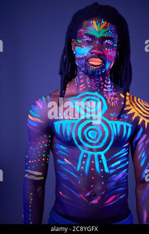 Bunte fluoreszierende Körperkunst mit ethnischen Drucken, junge männliche posiert bei der Kamera. Lumineszenz, Fluoreszenz, Körperkunst, Modelmodell Stockfoto