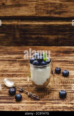 Joghurt mit Heidelbeeren und Chiasamen. Gesundes und nützliches Frühstückskonzept. Reife Beeren, Minzblätter, silberner Löffel auf Holzbrettern Hintergrund, Cop Stockfoto