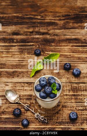Joghurt mit Heidelbeeren und Chiasamen. Gesundes und nützliches Frühstückskonzept. Reife Beeren, Minzblätter, silberner Löffel auf Holzbrettern Hintergrund, oben Stockfoto