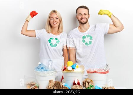 Fröhlicher junger Mann und Frau zeigen ihre muskulösen während hinter Recycling-Behälter stehen, Stärke. Nahaufnahme Porträt Stockfoto