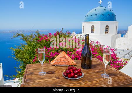 Wein und Kirschen für zwei auf dem Hintergrund des Meeres und der Insel Santorini. Stockfoto