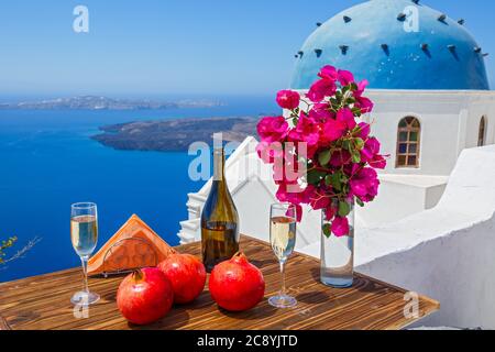 Wein und Granatapfel für zwei Personen auf dem Hintergrund des Meeres und der Insel Santorini. Stockfoto