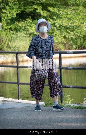 Eine ältere asiatisch-amerikanische Frau, die mit einer OP-Maske und Gummihandschuhen unterwegs ist. In einem Park in Flushing, New York. Stockfoto