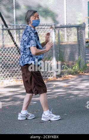 Eine ältere asiatische Amerikanerin, wahrscheinlich Chinesin, nimmt an einem Tai Chi Kurs im Freien Teil, während sie eine chirurgische Maske trägt. In Flushing, Queens, New York City. Stockfoto