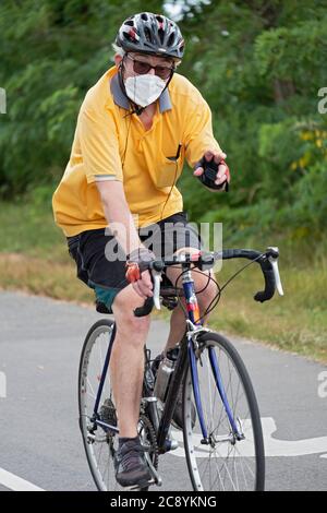 Ein fröhlicher Fahrradfahrer mit Maske und Helm winkt bei diesem Fotografen auf dem Radweg in der Nähe der Bayside Marina in Queens, New York City. Stockfoto