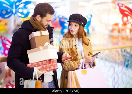 kaukasische rothaarige Frau und bärtiger Mann, frisch verheiratetes Paar diskutieren Einkaufen, Taschen in der Mall tragen Stockfoto