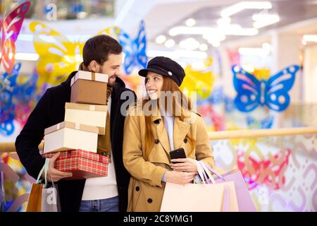 Porträt von jungen kaukasischen Paar adter Shopping in Mall, Mitte. Attraktive rothaarige weibliche und bärtige gutaussehende Mann zusammen mit Taschen Stockfoto