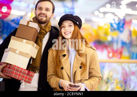 Porträt von jungen kaukasischen Paar adter Shopping in Mall, Mitte. Attraktive rothaarige weibliche und bärtige gutaussehende Mann zusammen mit Taschen Stockfoto