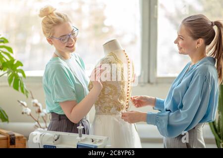 Zwei weibliche Mode Designer arbeiten zusammen am Arbeitsplatz in der Werkstatt zum Nähen von Kleidung, Brainstorming über neue Kleid Designs. Stockfoto