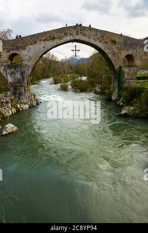 Touristen auf der fälschlicherweise als römische Brücke bezeichneten Brücke mit ihrem Kreuz Cruz de la Victoria, das an ihr über dem Fluss Sella hängt (Cangas de Onís, Asturien, Spanien) Stockfoto