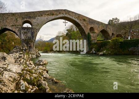 Die römische Brücke mit dem Kreuz Cruz de la Victoria, Symbol von Asturien, die über dem Fluss Sella (Cangas de Onís, Asturien, Spanien) hängt Stockfoto