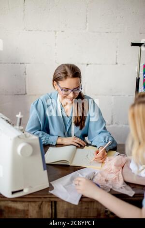 Es ist immer eine schöne Überraschung, die Sie in meinem Atelier zu erhalten. Junge Frau Unternehmer eröffnet sich eine maßgeschneiderte Anpassung shop, holding Skizze mit neuen Fa Stockfoto