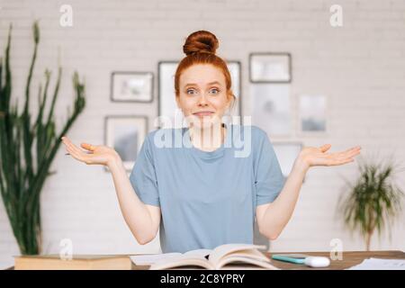 Glücklich überrascht Rothaarige junge Studentin sitzt an einem Tisch mit Lehrbüchern und einem Arbeitsbuch Stockfoto