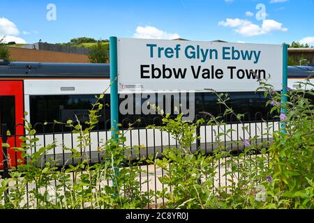 Ebbw Vale, Wales - Juli 2020: Bord mit Bahnhofsnamen am Bahnhof Ebbw Vale Town. Ein Zug ist im Hintergrund. Stockfoto