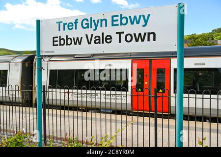 Ebbw Vale, Wales - Juli 2020: Bord mit Bahnhofsnamen am Bahnhof Ebbw Vale Town. Ein Zug ist im Hintergrund. Stockfoto