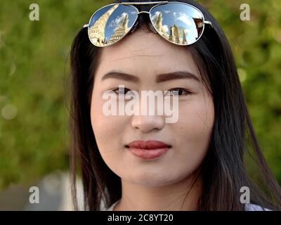 Die junge asiatische Touristin trägt eine Spiegelsonnenbrille (mit der Spiegelung von Bangkoks Wat Arun) auf ihrem Kopf und posiert für die Kamera. Stockfoto