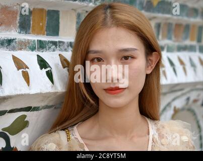 Junge chinesische Touristin mit gefärbten Haaren posiert für die Kamera im berühmten Wat Arun Tempel in Bangkok. Stockfoto