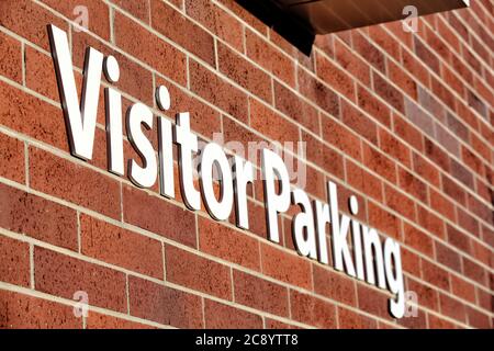 Ein weißes Besucherparkschild in Blockbuchstaben, auf einer roten Ziegelmauer, führt die Besucher zu einem reservierten Parkplatz. Stockfoto