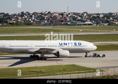 Eine Boeing 777-222ER (Reg N788UA), die von einem Rückzugschlepper auf einem der Rollwege von Sao Paulo/Guarulhos Intl. Flughafen vor Abflug. Stockfoto