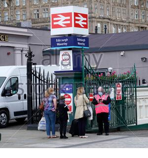 Menschen, die Gesichtsmasken tragen und mit einem Scotrail-Mitarbeiter in einer Hi-viz-Jacke vor der Waverley Station in Edinburgh sprechen Stockfoto