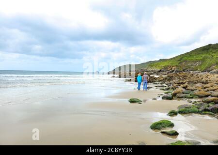 Zwei Personen gehen am Strand in Ost-Portholland mit wolkenblauem Himmel und Horizont über dem Wasser Stockfoto