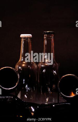 Bild im Hochformat von zwei transparenten Flaschen mit weißen und schwarzen Kappen, platziert unter anderen Flaschen unter einem dunklen Hintergrund gestapelt. Stockfoto