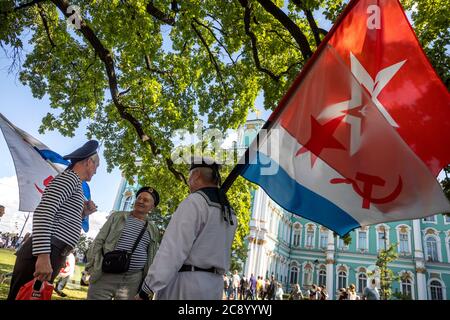 St. Petersburg, Russland - 26. Juli 2020 Männer mit der Navy Flagge der UdSSR nehmen an der Feier des Navy Day , auf dem Hintergrund des Winterpalastes in der Innenstadt von St. Petersburg, Russland. Der Tag der Marine in Russland wird jährlich am letzten Sonntag im Juli gefeiert Stockfoto