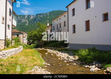 Der Fluss Pasji Rep, der an historischen Gebäuden im Zentrum des Dorfes Podnanos im Vipava-Tal, Gemeinde Vipava, Primorska, Slowenien, vorbeifließt Stockfoto