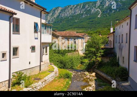 Der Fluss Pasji Rep, der an historischen Gebäuden im Zentrum des Dorfes Podnanos im Vipava-Tal, Gemeinde Vipava, Primorska, Slowenien, vorbeifließt Stockfoto