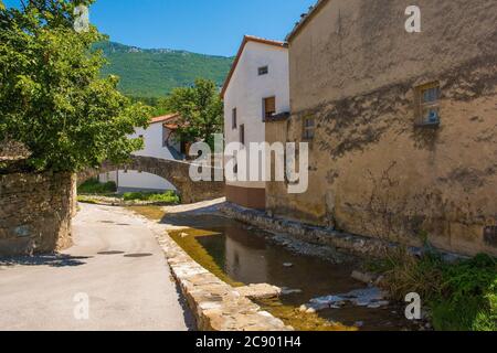 Der Fluss Pasji Rep, der an historischen Gebäuden im Zentrum des Dorfes Podnanos im Vipava-Tal, Gemeinde Vipava, Primorska, Slowenien, vorbeifließt Stockfoto