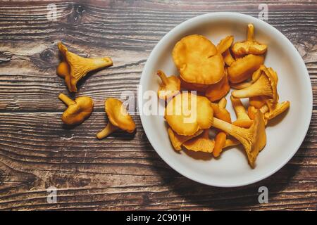 Waldpfifferlinge Pilze in einem weißen Teller auf einem braunen Hintergrund. Neue Ernte, Draufsicht. Stockfoto