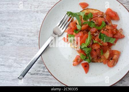 Bruschetta, italienische Vorspeise von geröstetem Brot mit Knoblauch und Olivenöl, serviert mit gewürfelten Tomaten und Basilikum auf einem Teller und einem grauen Tisch mit Kopie s Stockfoto