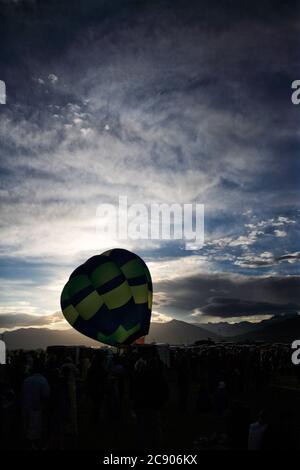 Ein Blick auf einen Heißluftballon, der aufgeblasen wird, und die Sonne beginnt über den Bergen aufzugehen. Stockfoto