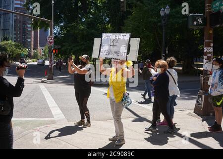 Eine Mutter Protesterin in gelben Posen für einen Videofilmer vor dem Bundesgericht Gebäude in der Innenstadt von Portland, Oregon, am Samstag, 25. Juli 2020. Stockfoto